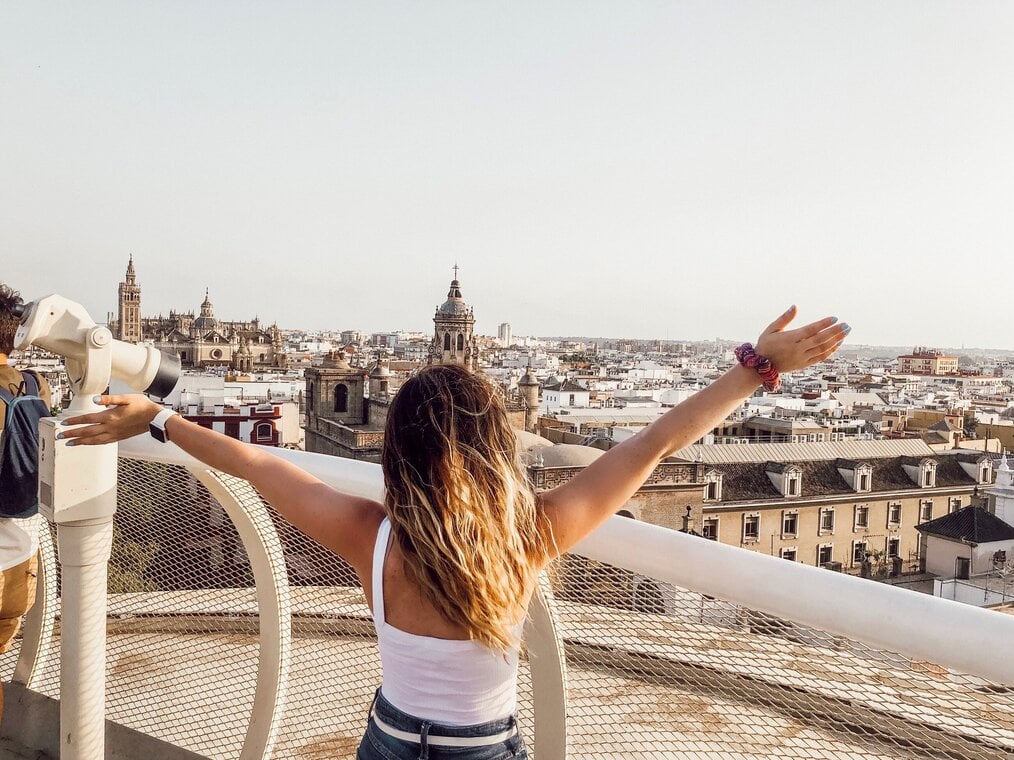 Person standing on top of balcony with hands up looking at city